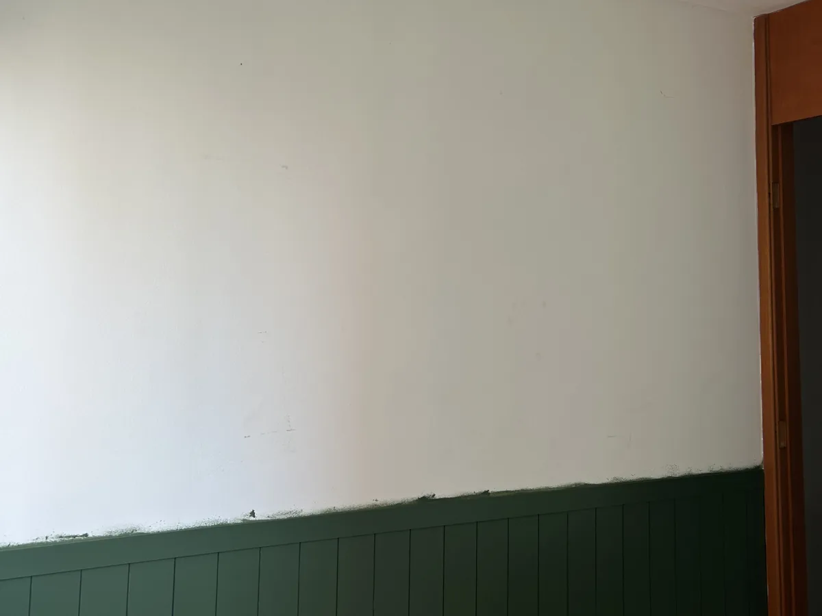 Parede branca acima do painel verde, com batente de madeira à direita