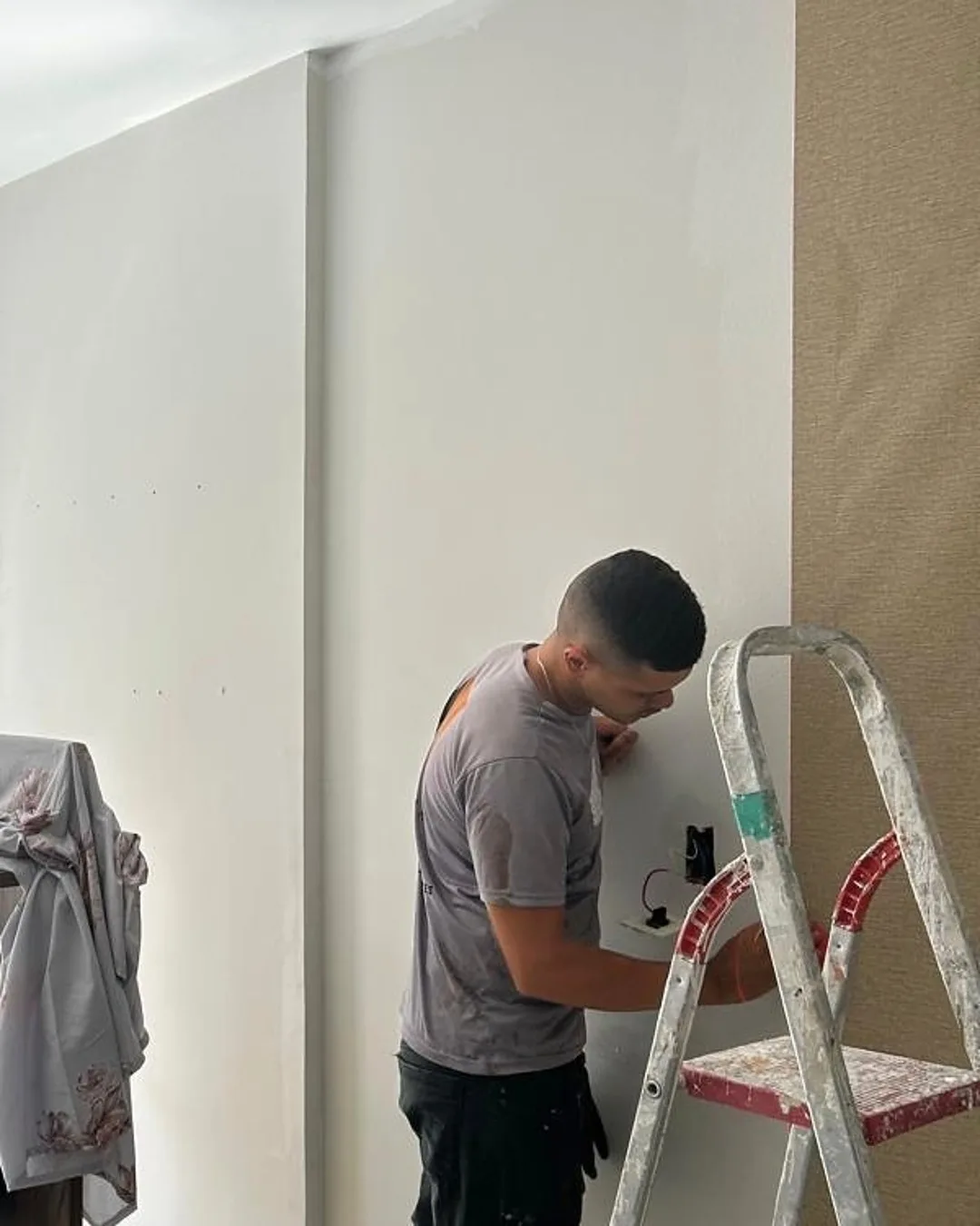 Profissional trabalhando na parede de um apartamento em Maceió, com o móvel coberto ao lado
