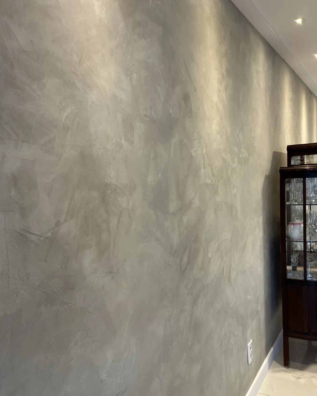 Acabamento decorativo cinza em parede de sala, com marcas do efeito visíveis sob a iluminação