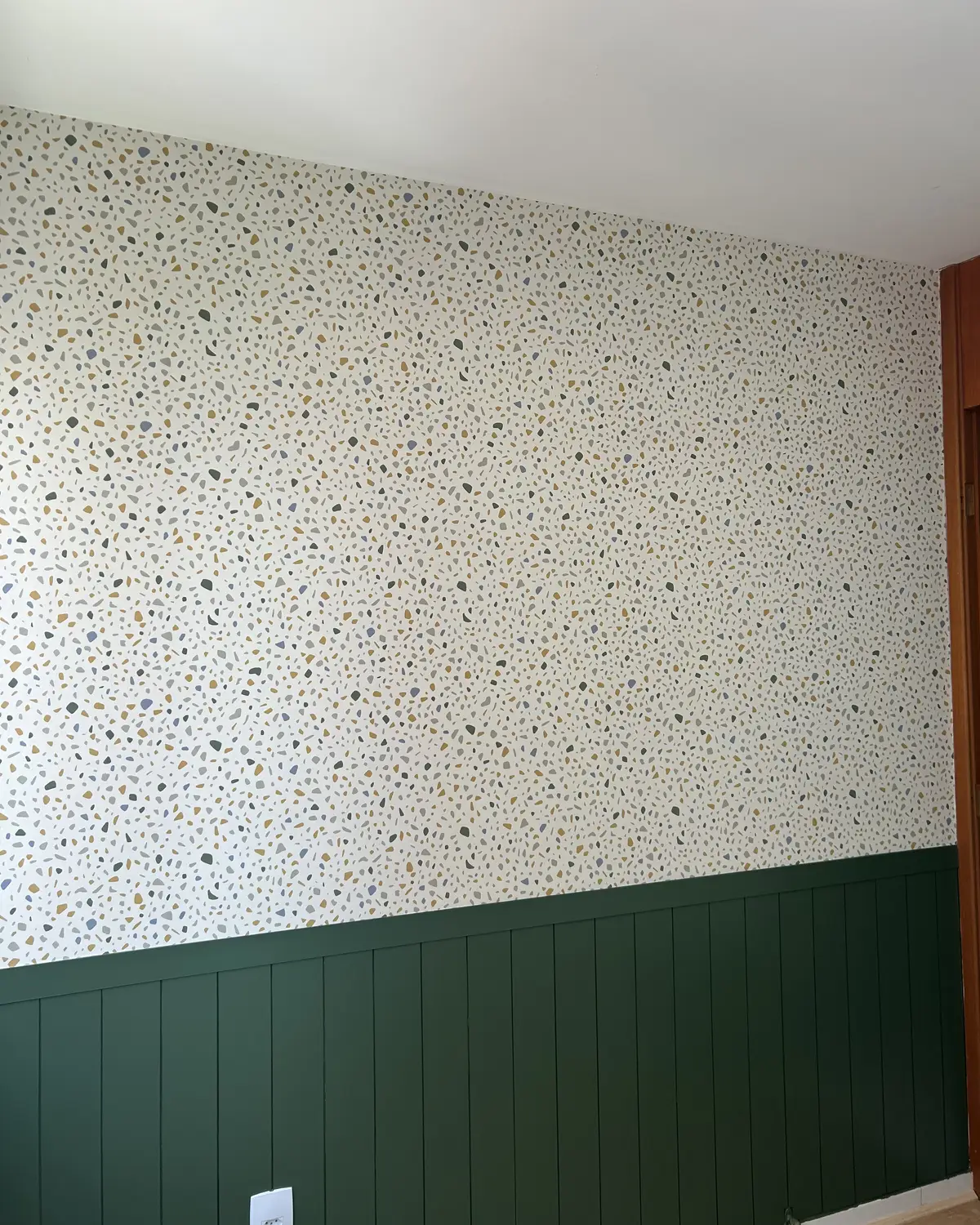 Papel de parede com padrão de granilite acima da meia parede verde de um quarto