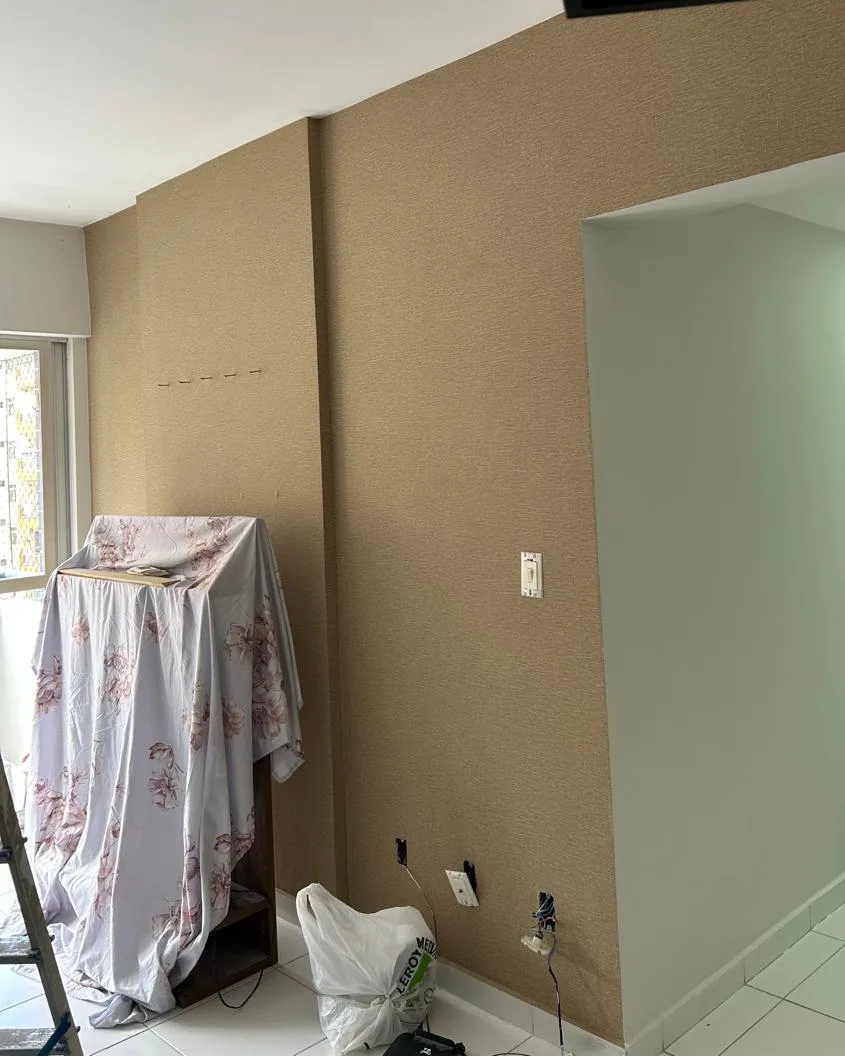 Parede de sala com textura decorativa em tom areia, com o móvel do cliente coberto por lençol durante o serviço